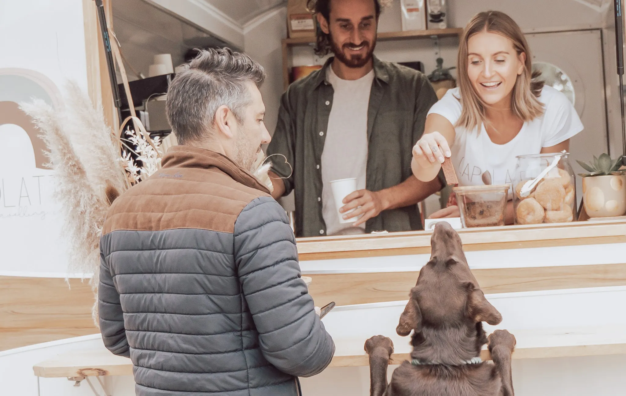 Capolatte staff handing coffee to a customer and dog at the caravan service window